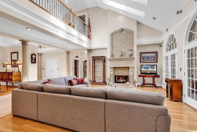 living room with high vaulted ceiling, a premium fireplace, light hardwood / wood-style floors, and decorative columns