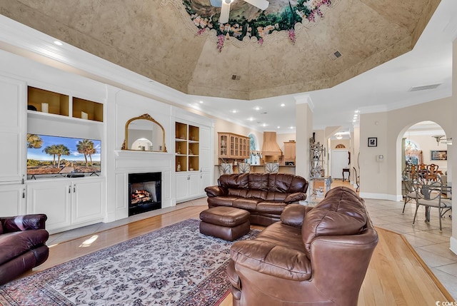 living room with built in shelves, a large fireplace, ornamental molding, and a tray ceiling