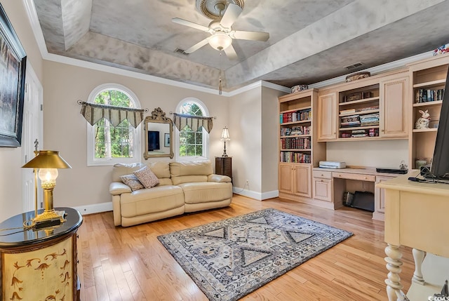 living room with built in desk, ornamental molding, a raised ceiling, ceiling fan, and light hardwood / wood-style floors