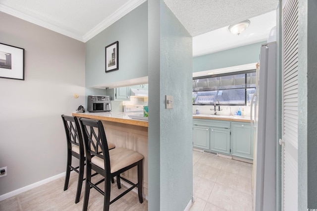 kitchen featuring butcher block counters, white refrigerator, crown molding, a textured ceiling, and light tile patterned flooring