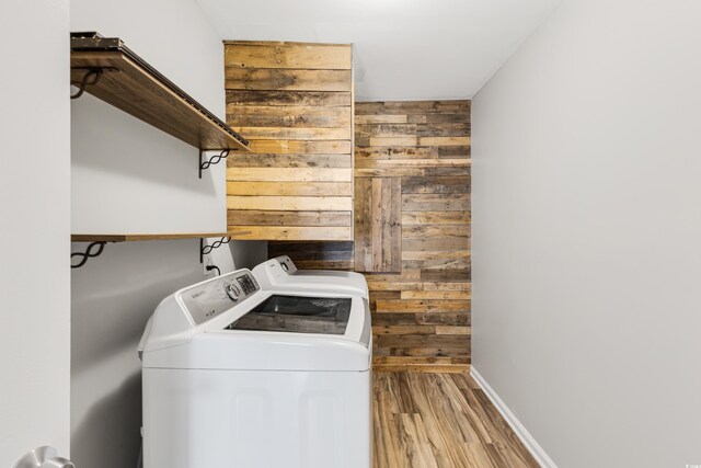 washroom featuring washing machine and clothes dryer, light wood-type flooring, and wood walls