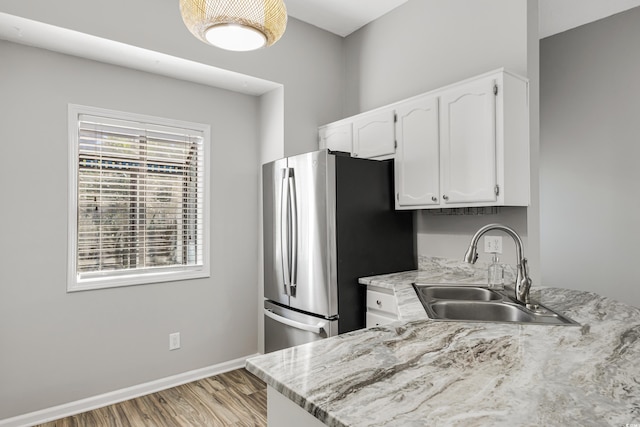 kitchen with sink, light wood-type flooring, white cabinetry, light stone counters, and stainless steel refrigerator