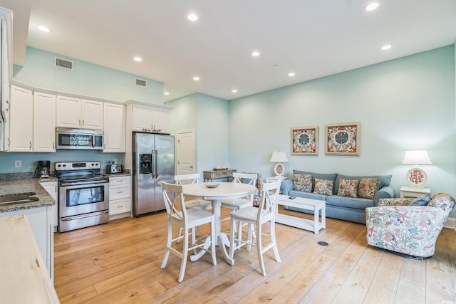 kitchen with white cabinetry, appliances with stainless steel finishes, dark stone counters, and light wood-type flooring