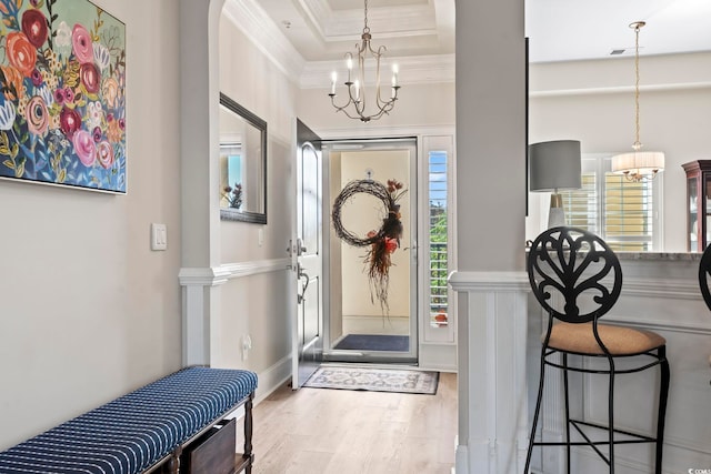 entryway featuring light hardwood / wood-style floors, a raised ceiling, ornamental molding, and an inviting chandelier