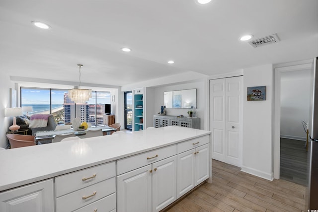 kitchen featuring white cabinetry, a chandelier, light wood-type flooring, and pendant lighting