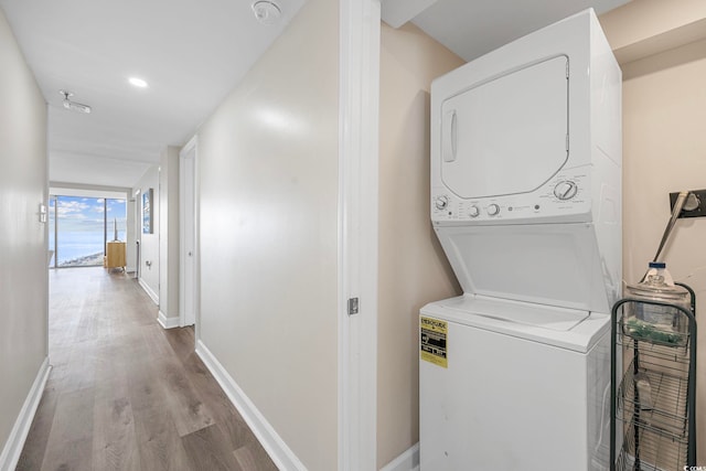 clothes washing area with stacked washing maching and dryer and light hardwood / wood-style flooring