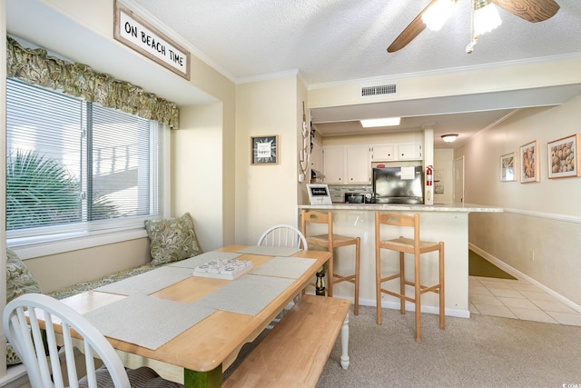 dining space featuring ceiling fan, light colored carpet, ornamental molding, and a textured ceiling