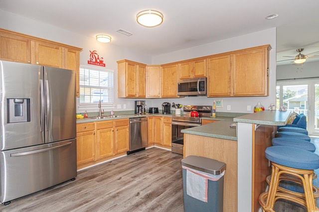 kitchen featuring kitchen peninsula, sink, a breakfast bar, light wood-type flooring, and appliances with stainless steel finishes