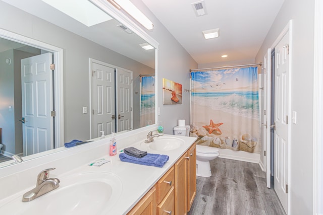 full bathroom featuring hardwood / wood-style flooring, toilet, shower / bath combo with shower curtain, a skylight, and vanity