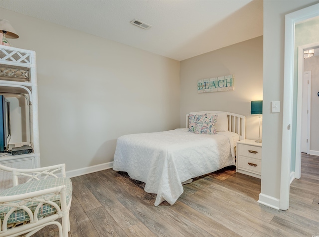 bedroom with baseboards, wood finished floors, and visible vents