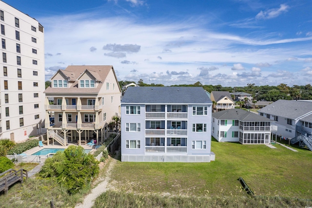 rear view of property featuring a yard, a sunroom, a community pool, and a balcony