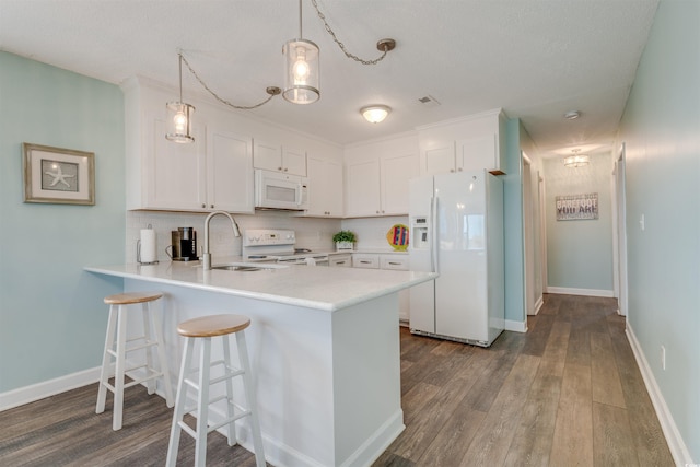 kitchen with a peninsula, a sink, dark wood finished floors, white appliances, and light countertops