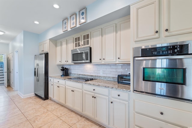 kitchen with appliances with stainless steel finishes, light tile patterned flooring, backsplash, white cabinetry, and light stone counters