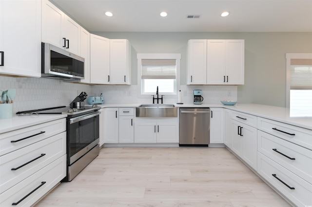 kitchen featuring white cabinetry, stainless steel appliances, sink, and light wood-type flooring