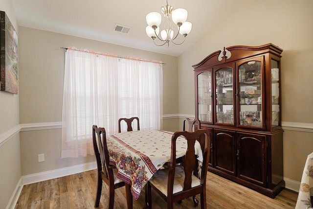 dining area with a chandelier, vaulted ceiling, and light hardwood / wood-style flooring