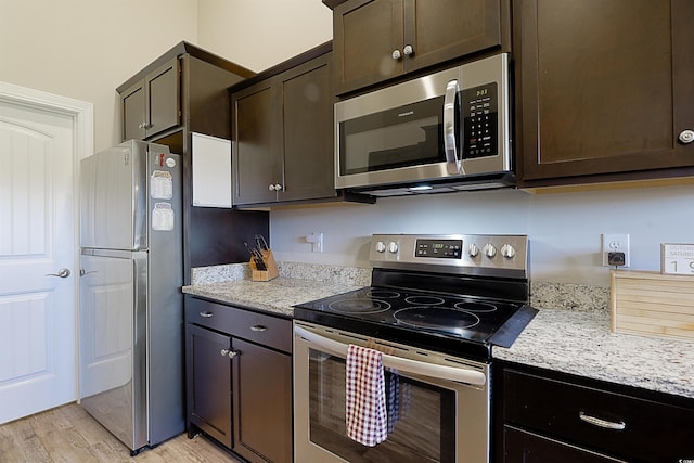 kitchen with dark brown cabinets, light stone countertops, appliances with stainless steel finishes, and light hardwood / wood-style flooring