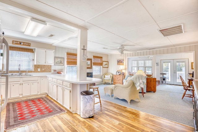 kitchen with french doors, kitchen peninsula, sink, ceiling fan, and white cabinetry