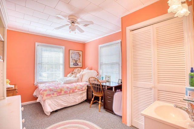 carpeted bedroom featuring a closet, ceiling fan, crown molding, and sink