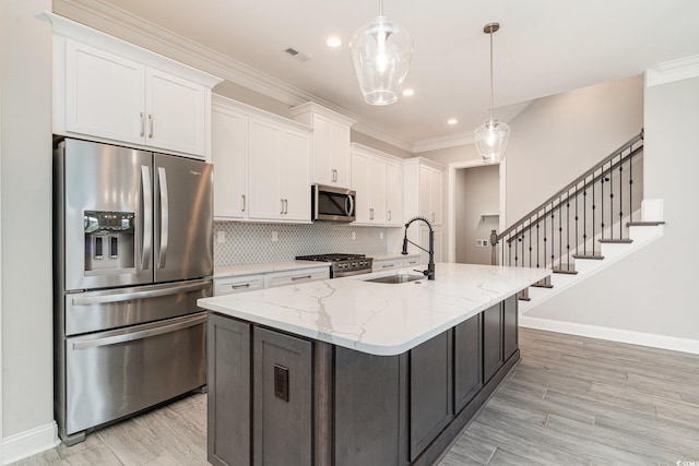 kitchen with light stone countertops, sink, stainless steel appliances, white cabinets, and a center island with sink