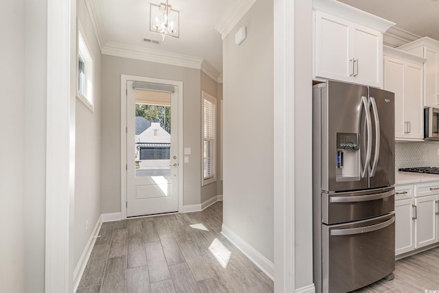 kitchen featuring stainless steel appliances, backsplash, ornamental molding, light wood-type flooring, and white cabinets