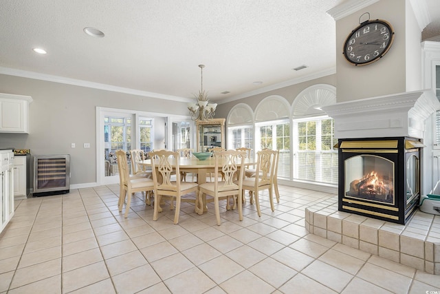 tiled dining room with a textured ceiling, wine cooler, ornamental molding, an inviting chandelier, and a multi sided fireplace