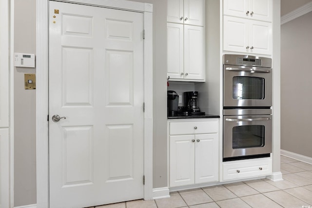 kitchen with stainless steel double oven, white cabinetry, crown molding, and light tile patterned floors