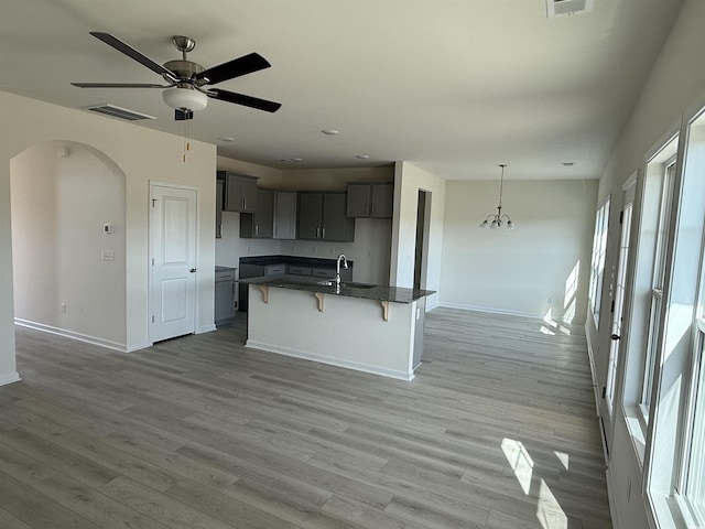 kitchen with gray cabinets, decorative light fixtures, an island with sink, sink, and a kitchen breakfast bar