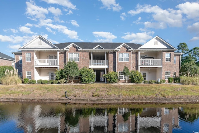 view of front of home with a balcony, a front lawn, and a water view