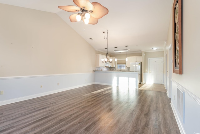 unfurnished living room featuring vaulted ceiling, dark hardwood / wood-style flooring, and ceiling fan with notable chandelier