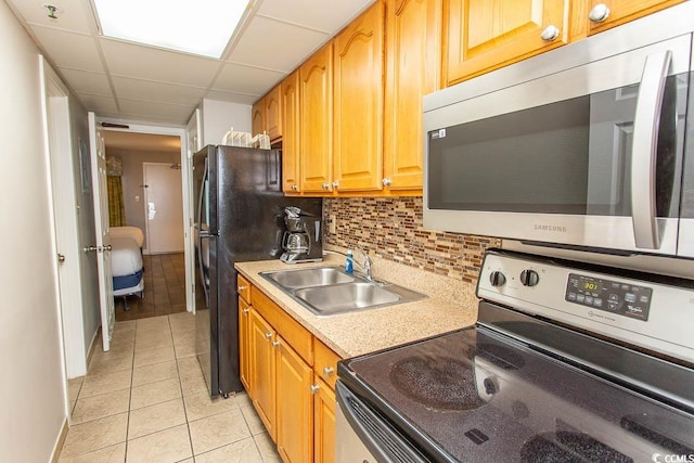 kitchen featuring appliances with stainless steel finishes, light tile patterned flooring, sink, backsplash, and a paneled ceiling