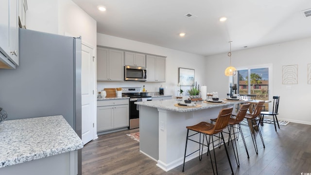 kitchen with a center island, appliances with stainless steel finishes, hanging light fixtures, and dark hardwood / wood-style floors