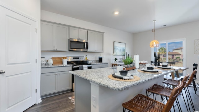 kitchen featuring appliances with stainless steel finishes, light stone counters, hanging light fixtures, and dark hardwood / wood-style flooring