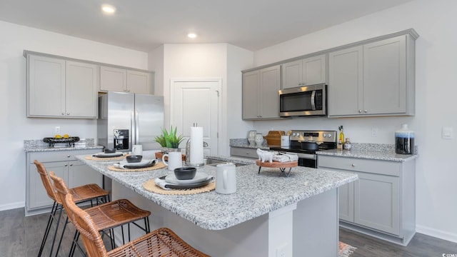 kitchen with gray cabinets, appliances with stainless steel finishes, a kitchen island with sink, and dark hardwood / wood-style floors