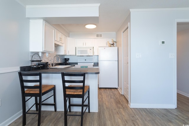 kitchen featuring a kitchen breakfast bar, kitchen peninsula, hardwood / wood-style floors, white cabinets, and white appliances