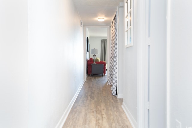 hallway with a textured ceiling and light wood-type flooring