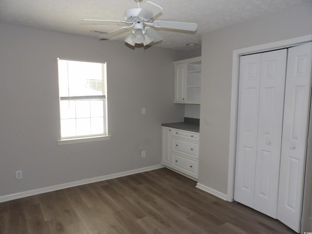 unfurnished bedroom featuring ceiling fan, a textured ceiling, a closet, and dark hardwood / wood-style flooring