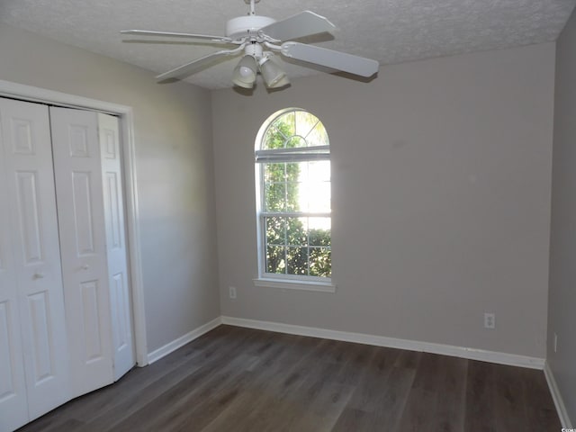 unfurnished bedroom with a closet, a textured ceiling, dark wood-type flooring, and ceiling fan