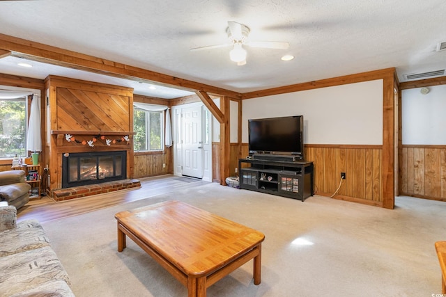 carpeted living area featuring healthy amount of natural light, wainscoting, a ceiling fan, a textured ceiling, and wooden walls