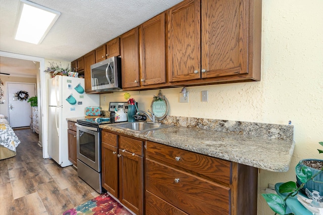 kitchen featuring dark wood-type flooring, sink, light stone countertops, appliances with stainless steel finishes, and a textured ceiling