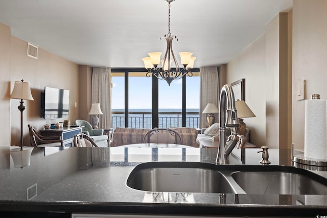 kitchen with dark stone counters, expansive windows, hanging light fixtures, sink, and a chandelier