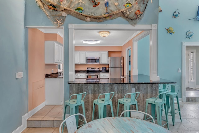 kitchen featuring appliances with stainless steel finishes, crown molding, white cabinetry, and dark stone counters