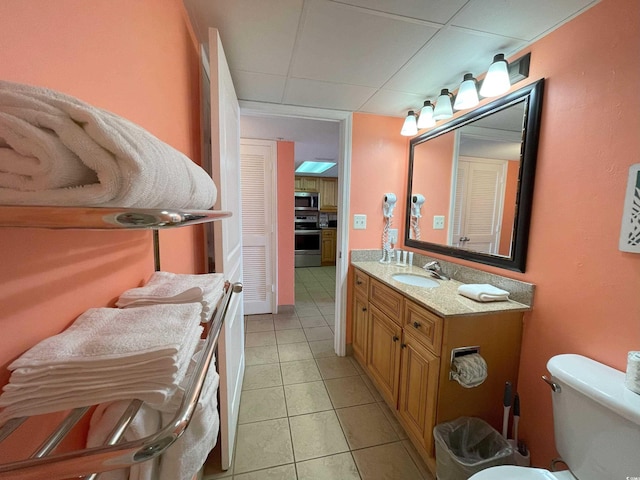 bathroom with a paneled ceiling, tile patterned flooring, vanity, and toilet