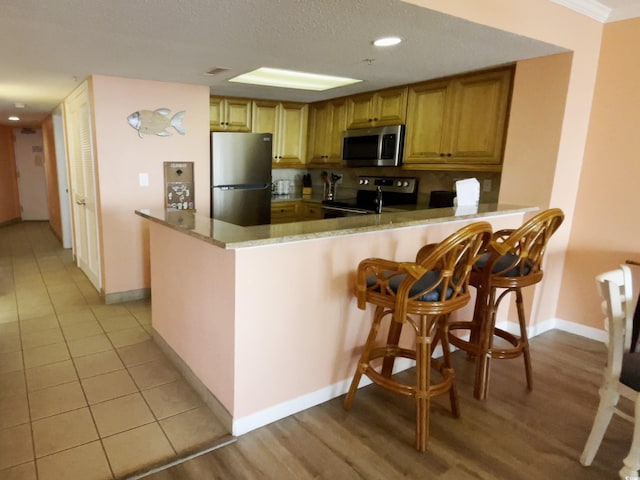 kitchen with a breakfast bar area, appliances with stainless steel finishes, crown molding, kitchen peninsula, and light tile patterned flooring