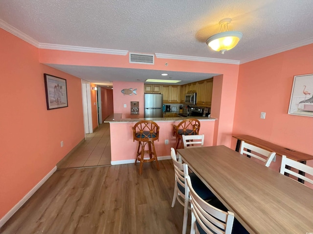 dining area featuring a textured ceiling, ornamental molding, and light hardwood / wood-style floors