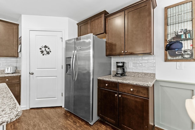 kitchen featuring dark wood-type flooring, dark brown cabinets, stainless steel fridge, light stone counters, and tasteful backsplash