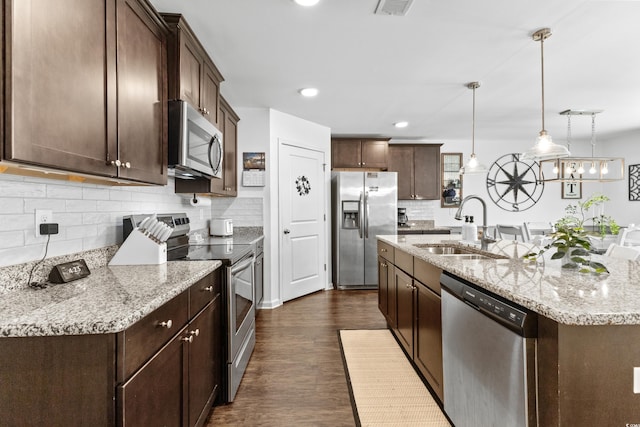 kitchen with sink, dark hardwood / wood-style flooring, stainless steel appliances, pendant lighting, and light stone counters