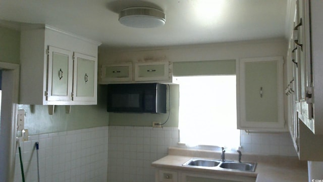 kitchen with light countertops, white cabinets, black microwave, and a sink