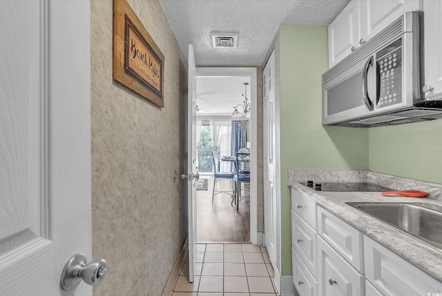 kitchen with a textured ceiling, black electric cooktop, white cabinetry, light stone counters, and light tile patterned floors