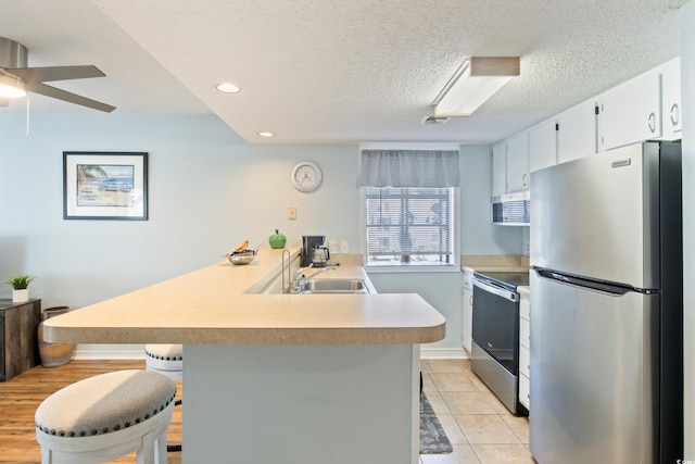 kitchen featuring a kitchen breakfast bar, kitchen peninsula, sink, white cabinetry, and appliances with stainless steel finishes