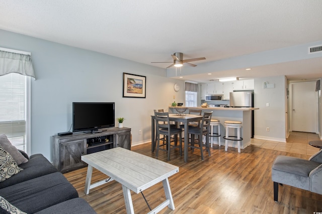 living room featuring a textured ceiling, light wood-type flooring, and ceiling fan